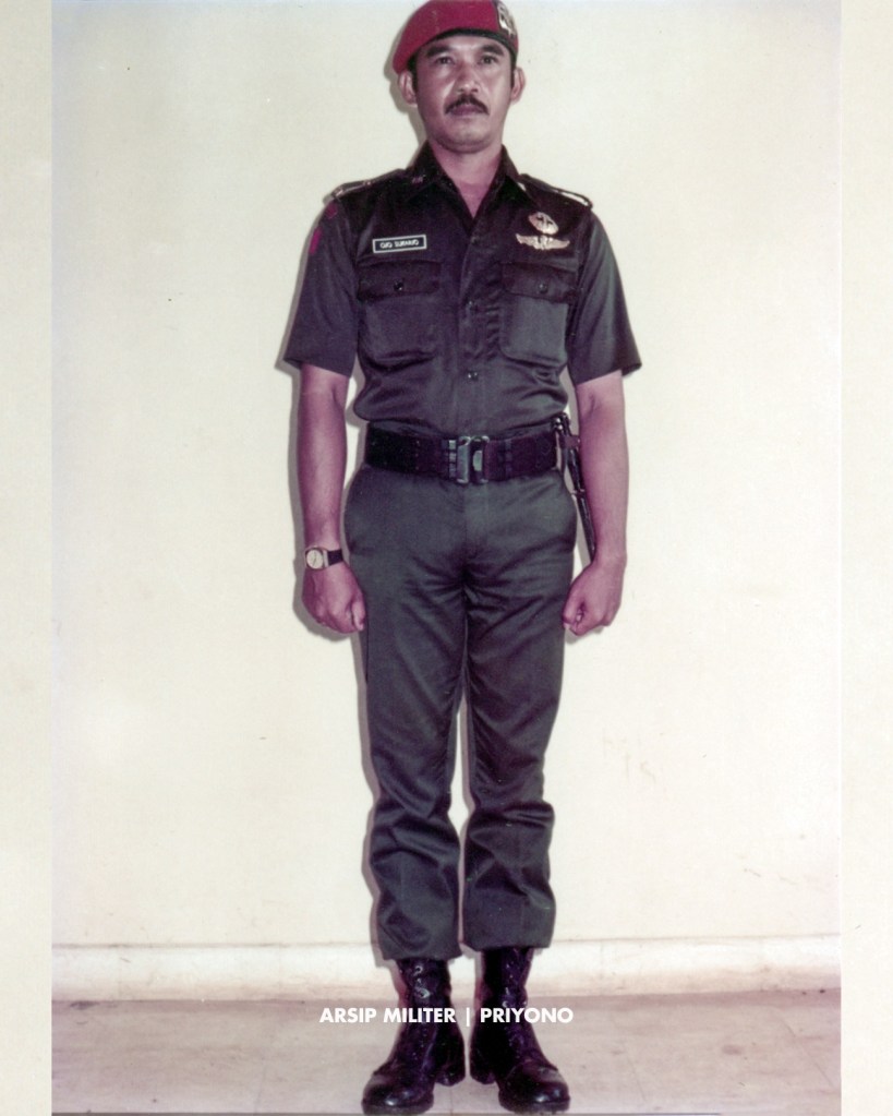 PDH hijau lengan pendek dengan baret KOPASSANDHA, brevet Komando dan wing terjun pinned, plat nama, 

Patch Para-Komando di lengan kiri, serta patch “MARKAS” dan scroll “KOMANDO” di lengan kanan.